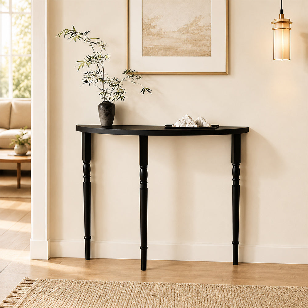 Black curved-front console table against a pale entryway wall, with a vase and decorative tray.