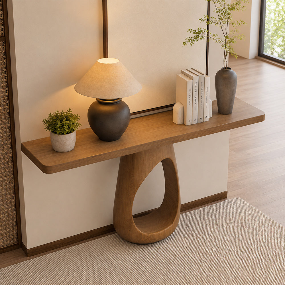 Brown wood-tone console table with a sculptural loop base, styled with a lamp, books and plants in an entryway.