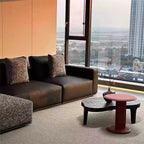Detail of the dark sofa seats, squared arm and contrasting textured back pillows beside a window.