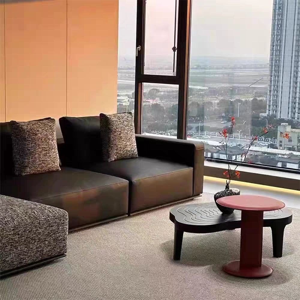 Detail of the dark sofa seats, squared arm and contrasting textured back pillows beside a window.