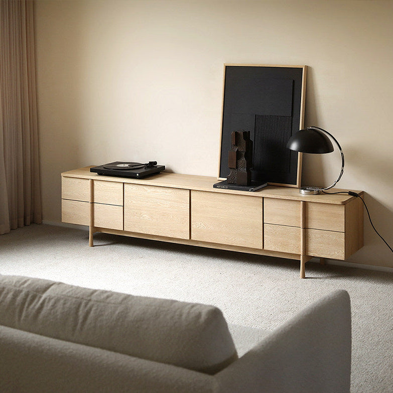 Light wood-tone storage TV stand against a wall in a living room, with a sofa in the foreground.