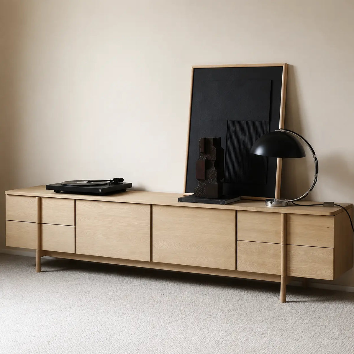 Angled view of the light wood-tone TV stand, showing its flat drawer fronts, cabinet doors and slender raised legs.