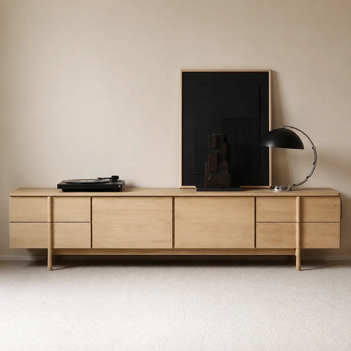 Light wood-tone TV stand on raised legs, with drawers and central cabinets, styled with a turntable and black lamp.