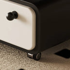 Detail of the coffee table's cream drawer front, dark round knob and small caster wheel.