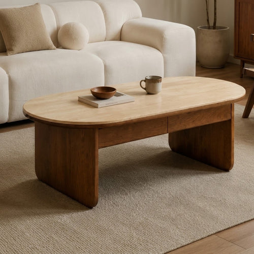 Oval coffee table with a light top, brown panel legs and slim drawer fronts beside a cream sofa.