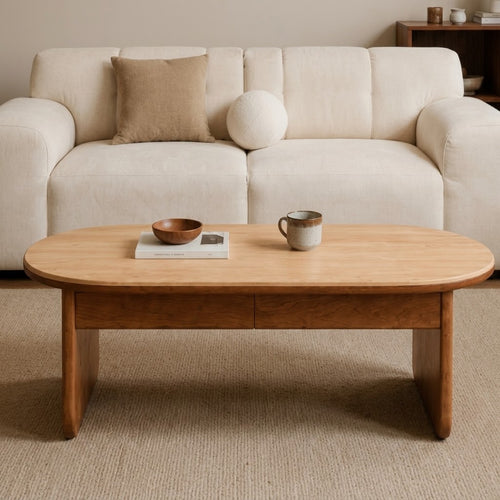 Front view of the oval coffee table with a light top, two drawer fronts and broad brown legs.