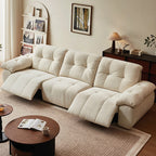 Angled room view of the cream reclining sofa with extended outer footrests and a closed center seat.