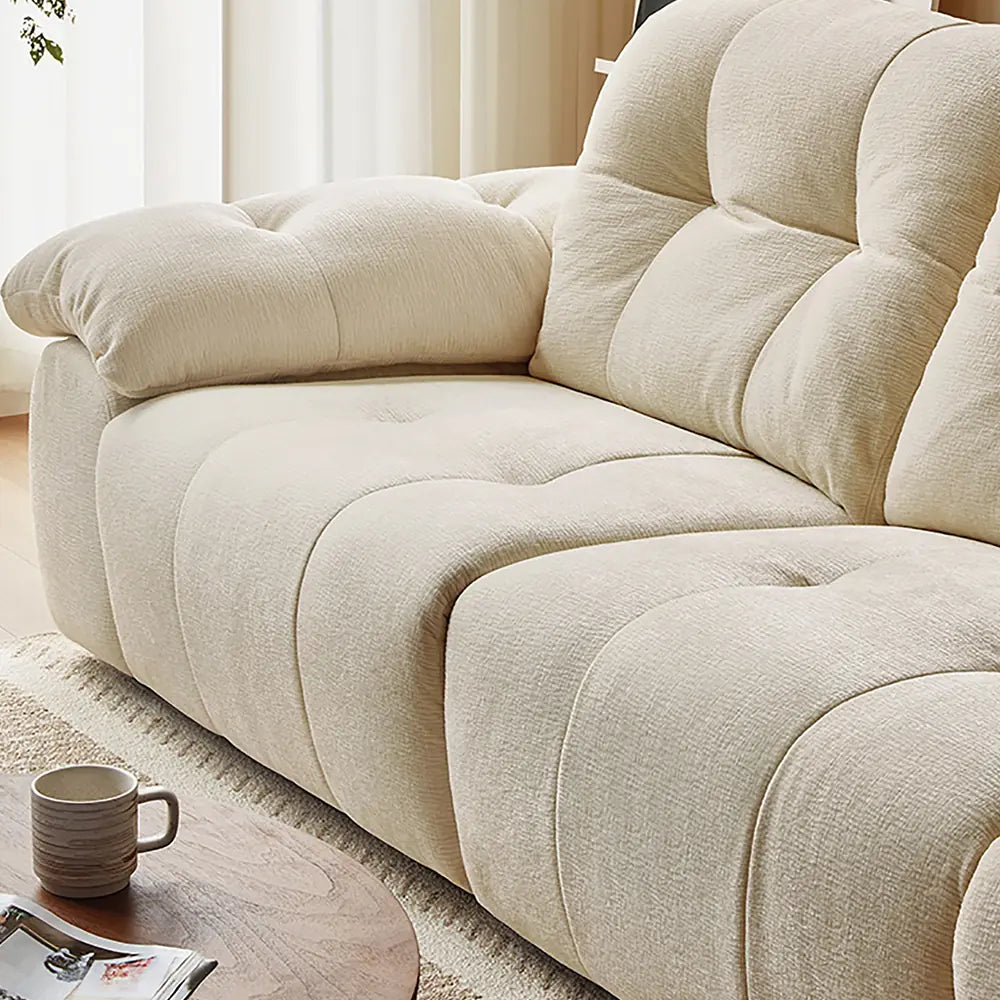 Detail of the cream reclining sofa's broad seat cushions and padded back upholstery.