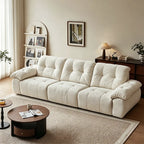 Cream reclining sofa with three padded back cushions and broad pillow arms in a living room.