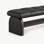 Angled detail of the black bench's rounded upholstered side support, stitched cushion and lower shelf.