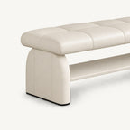 Angled detail of the cream bench's rounded upholstered side support, stitched cushion and lower shelf.
