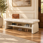 cream padded shoe bench with a stitched seat, broad upholstered supports and a lower shelf holding shoes.