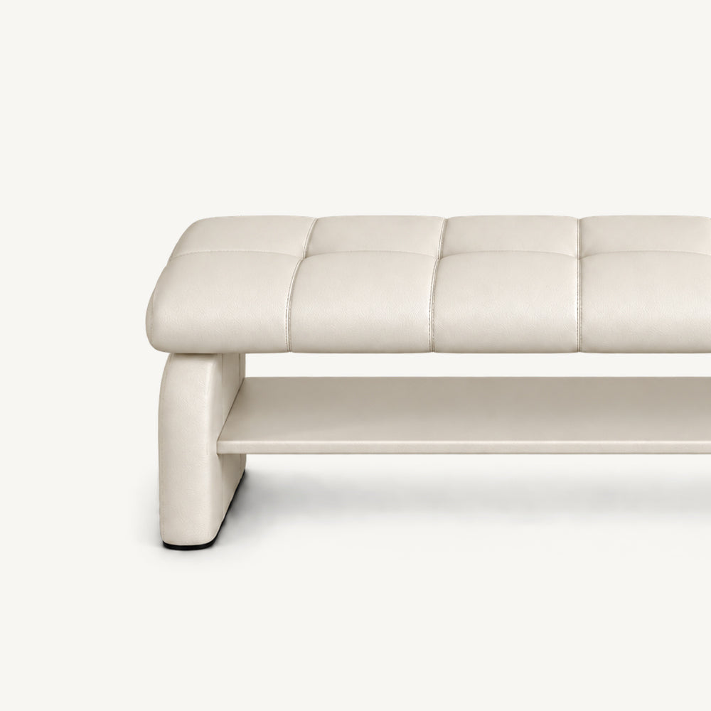 Close-up of the cream bench's stitched cushion, left side support and lower storage shelf.