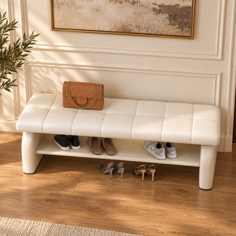 Overhead angled view of the cream bench's stitched cushion, broad side supports and shoe shelf.
