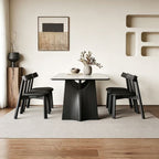 Pale rectangular dining table on sculptural black supports, viewed from the end between black chairs.