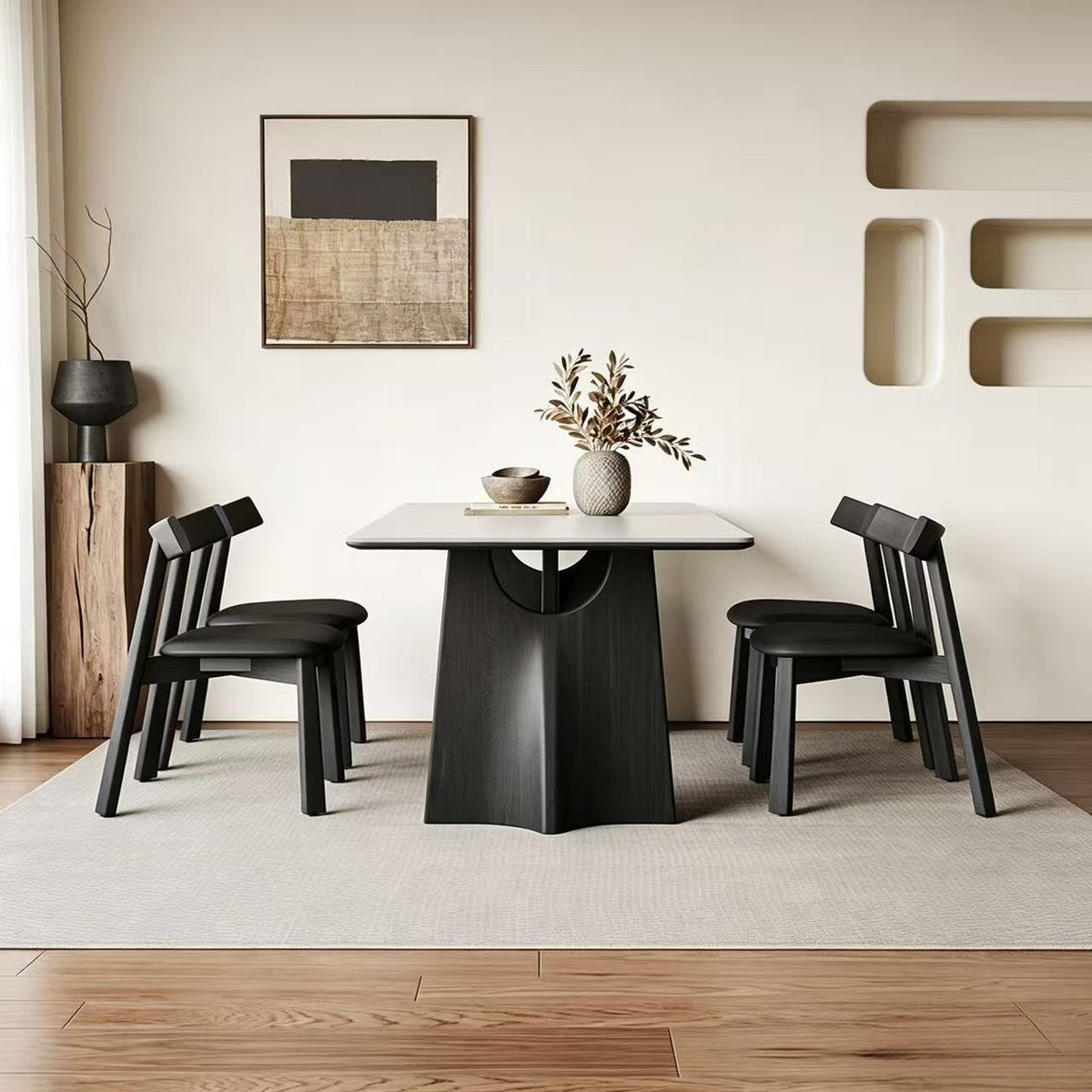 Pale rectangular dining table on sculptural black supports, viewed from the end between black chairs.
