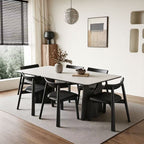 Pale rectangular dining table with black sculptural legs, surrounded by black chairs on a rug.