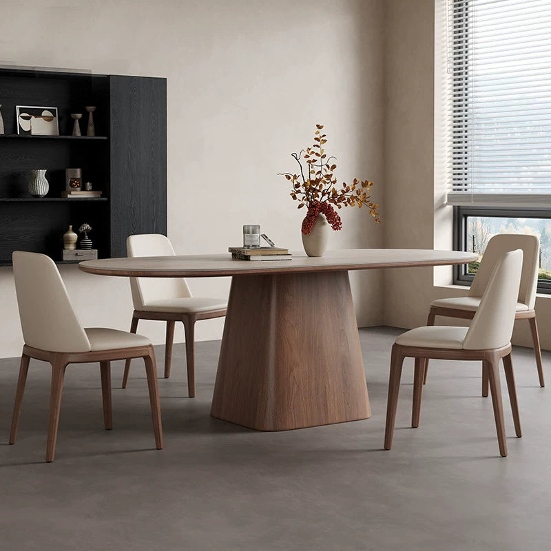 Pale oval dining table with a broad brown tapered pedestal, surrounded by cream upholstered chairs.