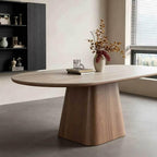 Pale oval dining table with a brown tapered central pedestal, styled with a vase and glass.