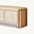 Close-up of the bench's rounded gold-tone side, beige cushion and pale beige patterned door.