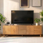 Light wood-tone TV stand with alternating smooth and horizontally ribbed fronts beneath a television.