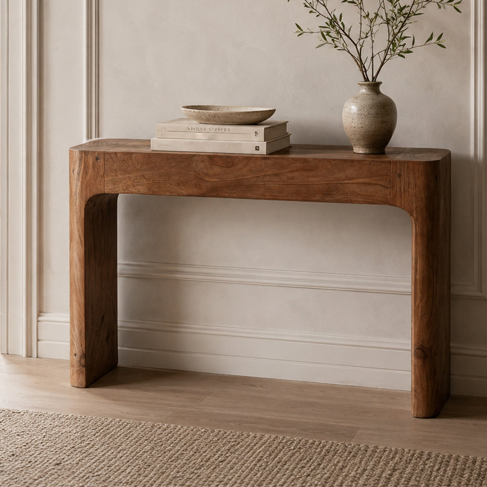 Brown narrow console table with rounded corners and visible grain, styled with books and a branch-filled vase.