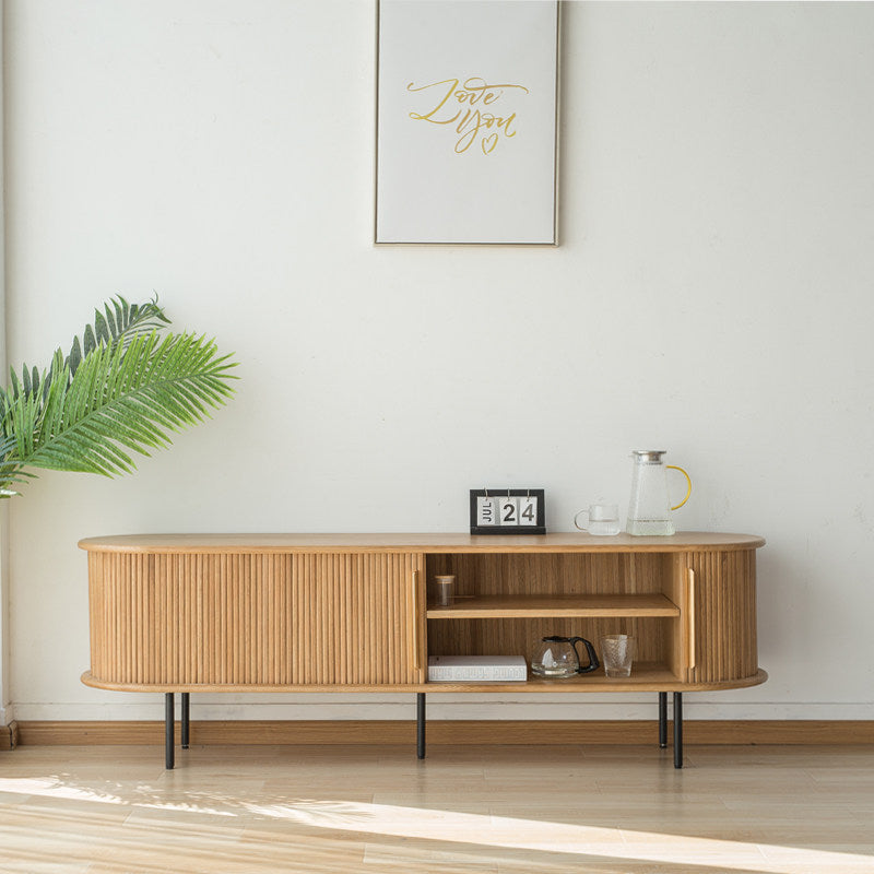Light wood-tone TV stand with a slatted door moved aside to reveal two open shelves.