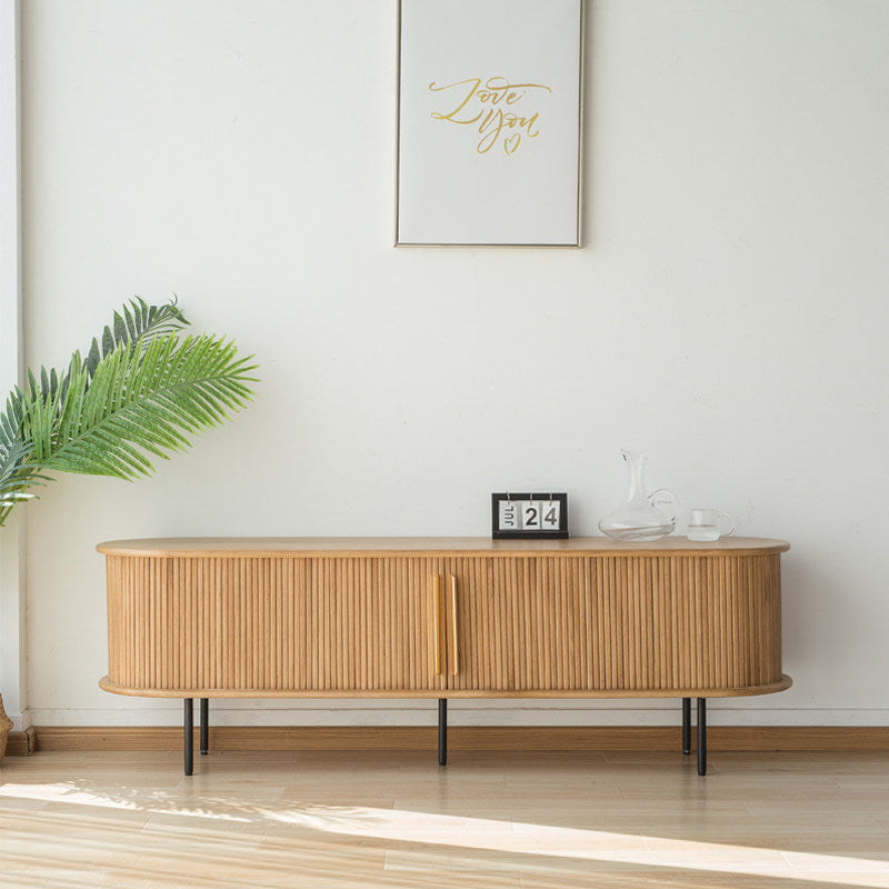 Light wood-tone TV stand with rounded ends, vertical slatted doors and slim black legs.