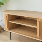 Close-up of the TV stand's open shelves and slatted doors curving around its rounded ends.