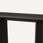 Front detail of the dark console table's smooth rounded top edge and two panel legs.