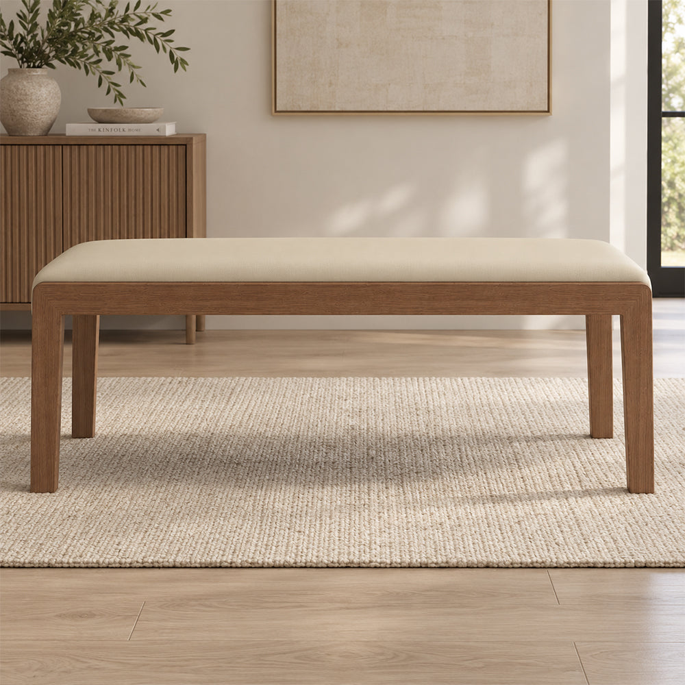 Front view of the cream padded bench seat above its brown frame and straight legs.
