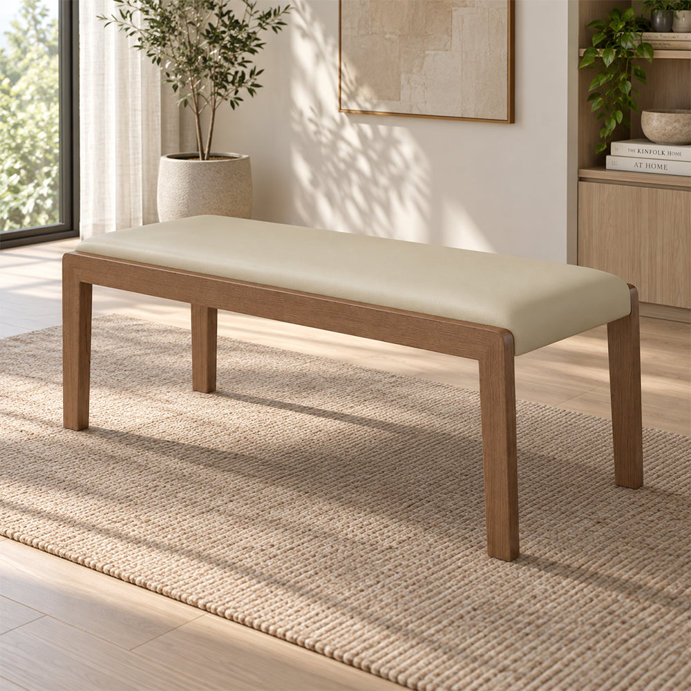 Cream upholstered bench with a brown rectangular frame and four slim legs in a bright room.