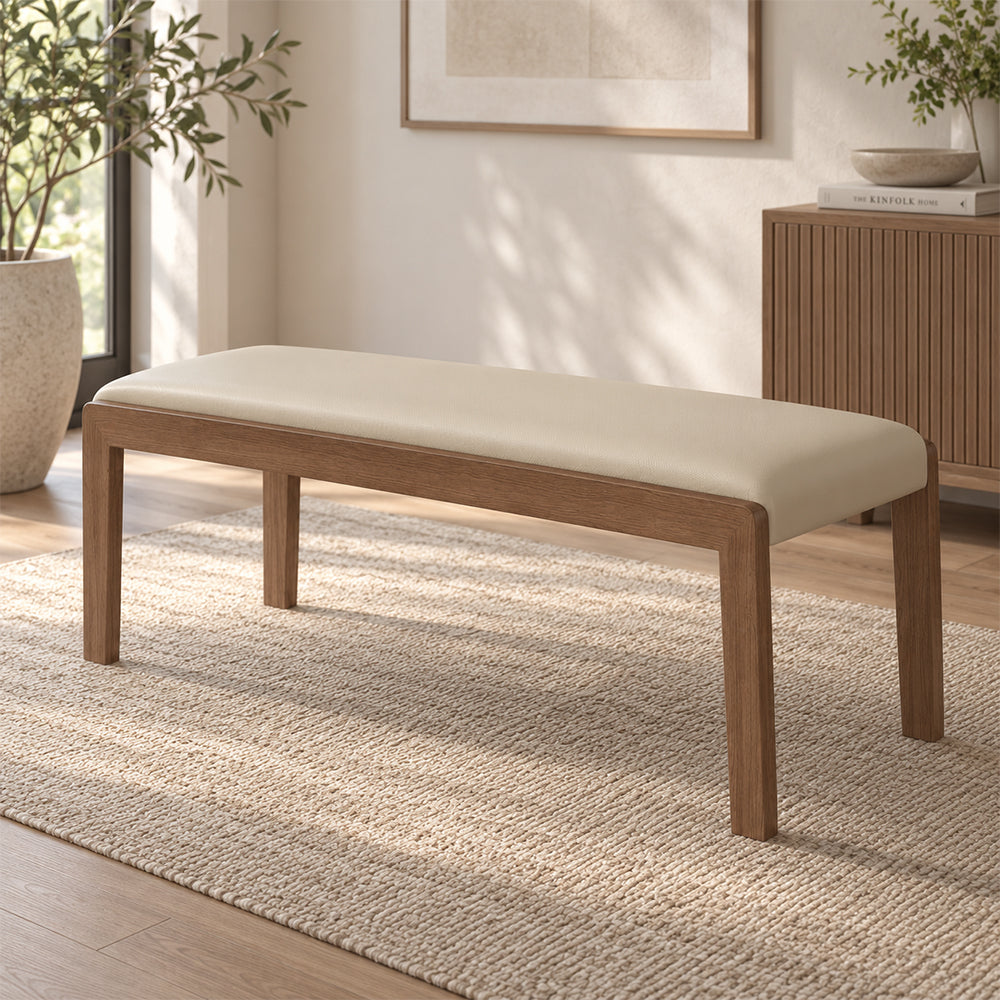 Angled room view of the cream upholstered bench with a slim wood-tone frame.