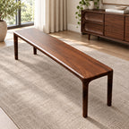 Long brown wood-grain bench with rounded corners and four slim legs on a woven rug.