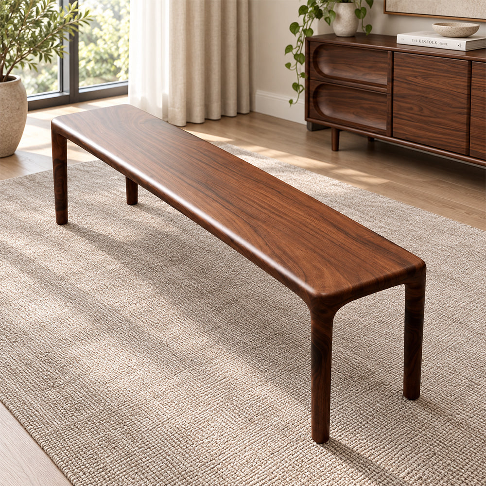 Long brown wood-grain bench with rounded corners and four slim legs on a woven rug.