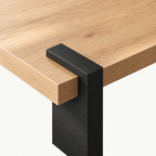 Overhead detail of a black support wrapping over the light wood-grain square tabletop edge.