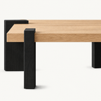 Side detail of the square coffee table's thick light wood-grain top and black supports.