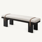 Cream upholstered dining bench with four black block legs and two brown straps across the seat.
