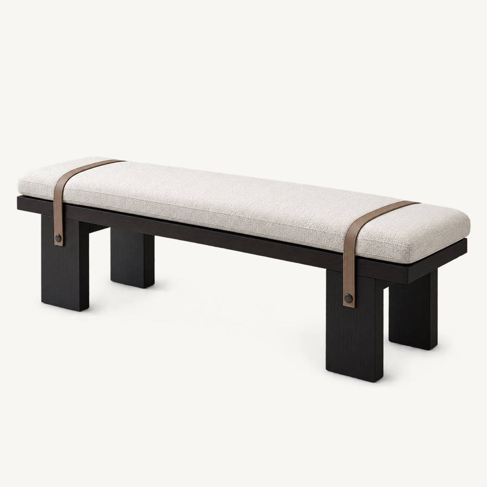 Cream upholstered dining bench with four black block legs and two brown straps across the seat.