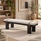 Cream upholstered bench with a black block-leg frame and two brown straps over the cushion.