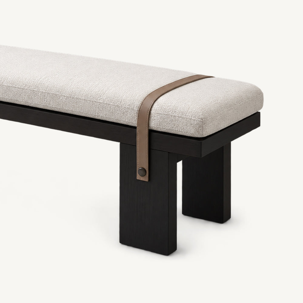 Angled detail of the bench's rounded cream cushion end, brown strap and black block legs.