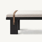 Close-up of a brown strap crossing the cream bench cushion and fastening to a black leg.