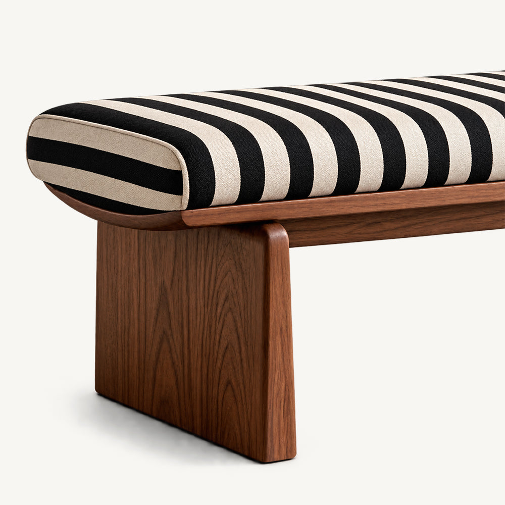 Angled detail of the bench's rounded striped cushion end, brown frame and panel leg.