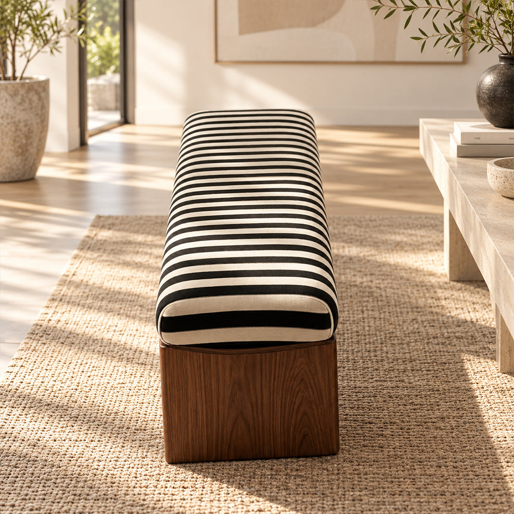 End view of the striped upholstered bench showing its rounded cushion and brown panel support.