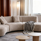 Front detail of the taupe sofa's curved center seats, loose cushions and patterned throw.