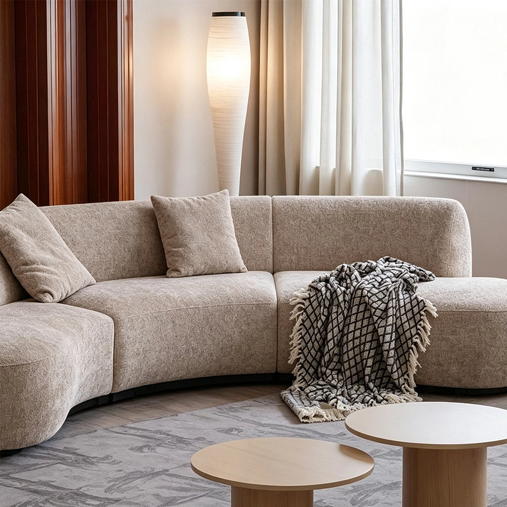 Front detail of the taupe sofa's curved center seats, loose cushions and patterned throw.