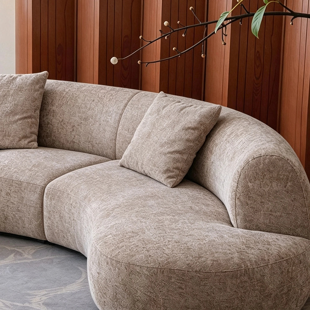 Close-up of the taupe sofa's rounded end seat, curved back and accent pillow.