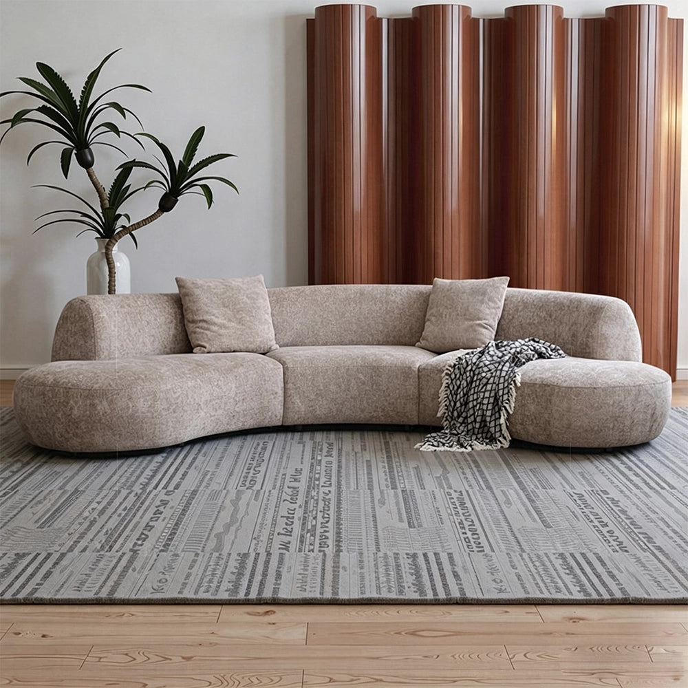 Taupe curved modular sofa with rounded end seats, loose cushions and a patterned throw.