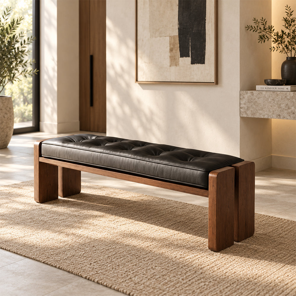 Bench with a black tufted cushion and brown split-panel legs in a sunlit entryway.