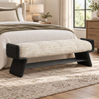 cream upholstered bench with a black frame and open shoe rack at the foot of a bed.